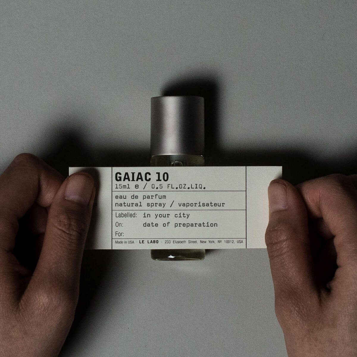 Le Labo Gaiac 10 eau de parfum bottle held in two hands, hand-written label