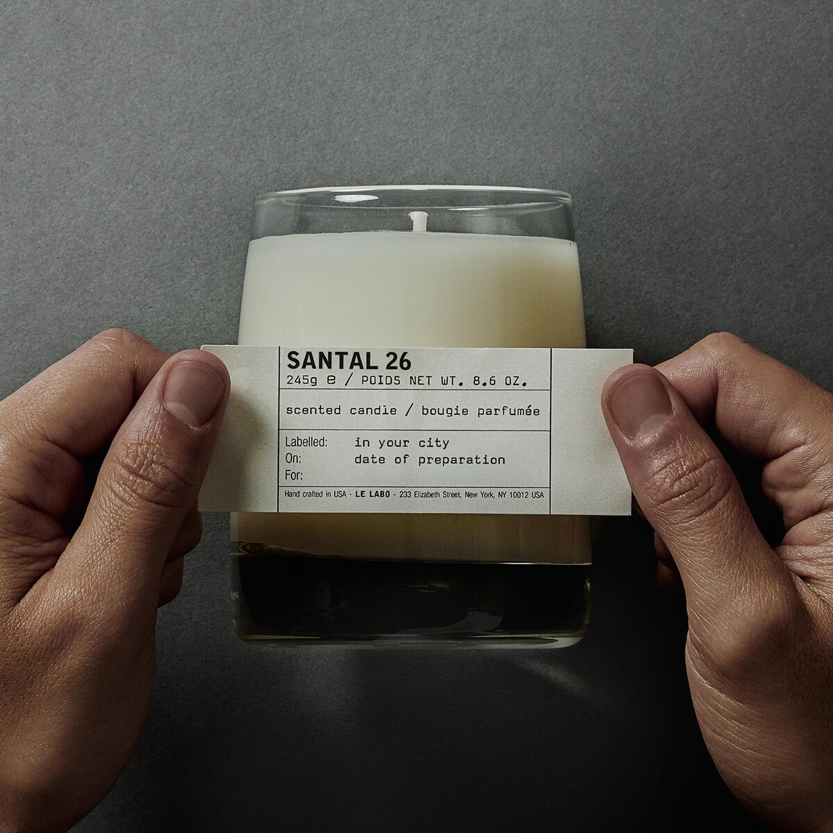 Le Labo Santal 26 classic candle held in two hands, hand-written label
